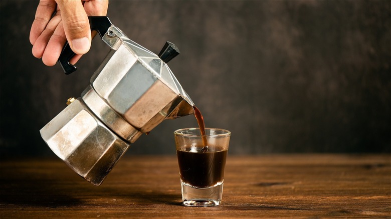 A hand pouring coffee from a moka pot