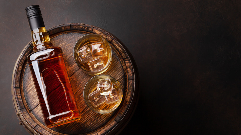 Label-free bourbon bottle next to two glasses of bourbon on wooden tray