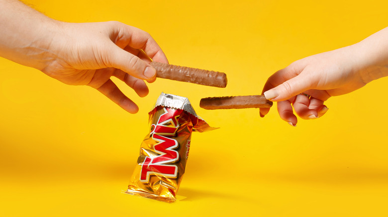Two hands, each holding a Twix bar