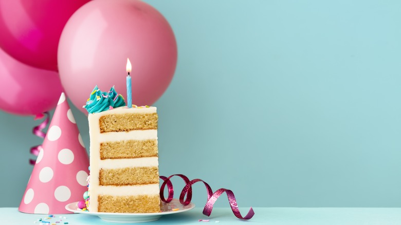 Vanilla birthday cake with a lit candle, next to a party hat