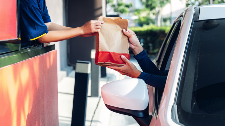 Employee at fast food restaurant hands a customer their order in the drive thru
