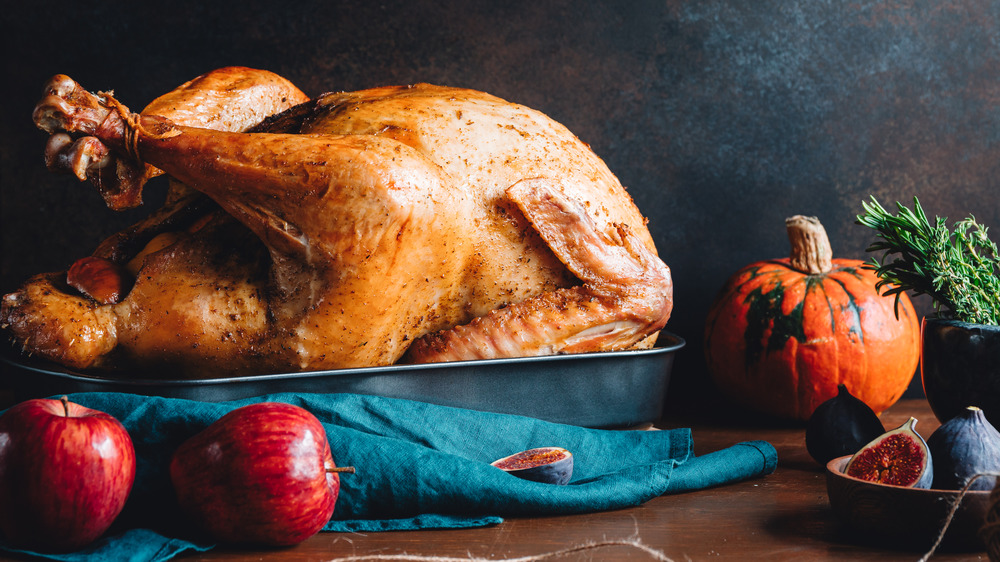 Cooked turkey on table with apples, figs, herbs, and squash