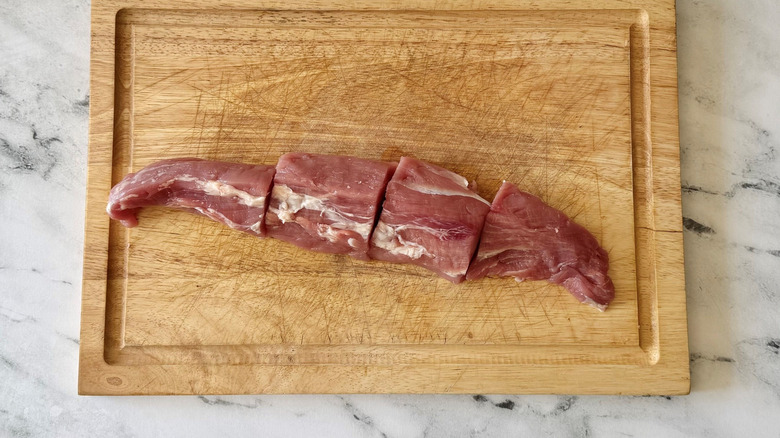 Pork tenderloin slices into four pieces on wooden board