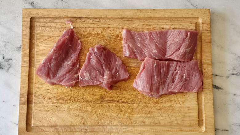 Butterflied pork tenderloin pieces on wooden board