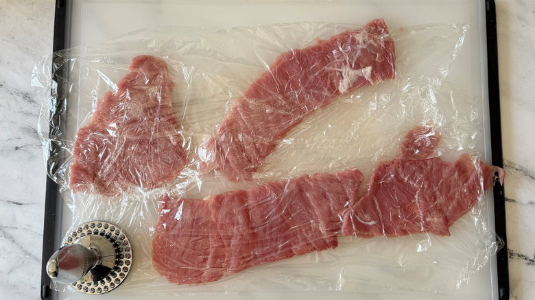 Pounded tenderloin pieces under plastic wrap with meat mallet