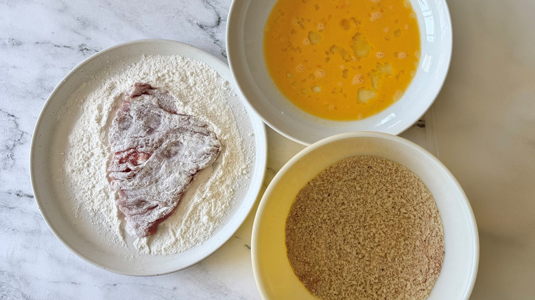 Bowl of beaten egg, breadcrumbs, and flour with pork tenderloin in it