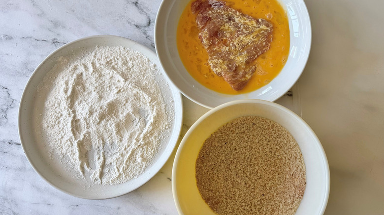 Bowls of flour, breadcrumbs, and egg with pork tenderloin in it