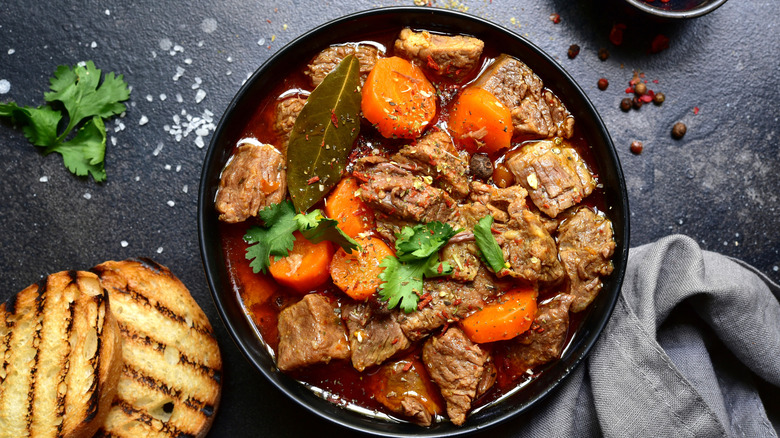 A plate of beef stew next to two slices of grilled bread.