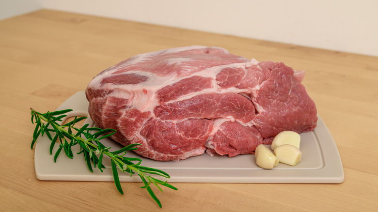 Raw chuck roast next to garlic and rosemary on cutting board.