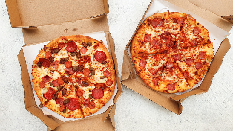 Two meat and cheese pizzas in open pizza boxes.
