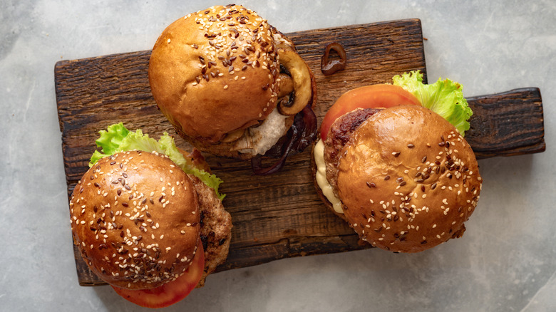 Three different burgers arranged on dark wood cutting board on counter