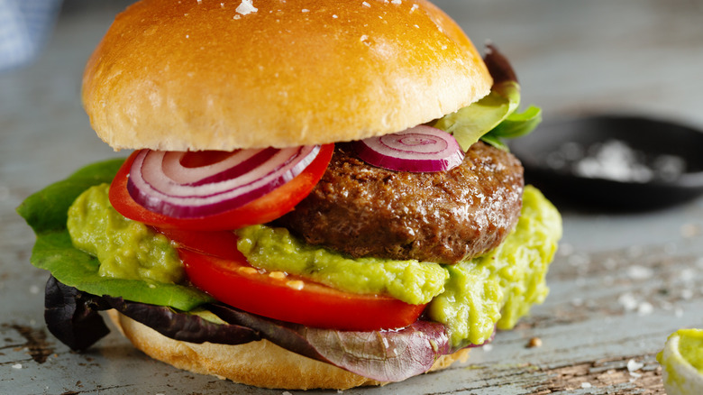 Burger with guacamole, tomatoes, lettuce, and red onion