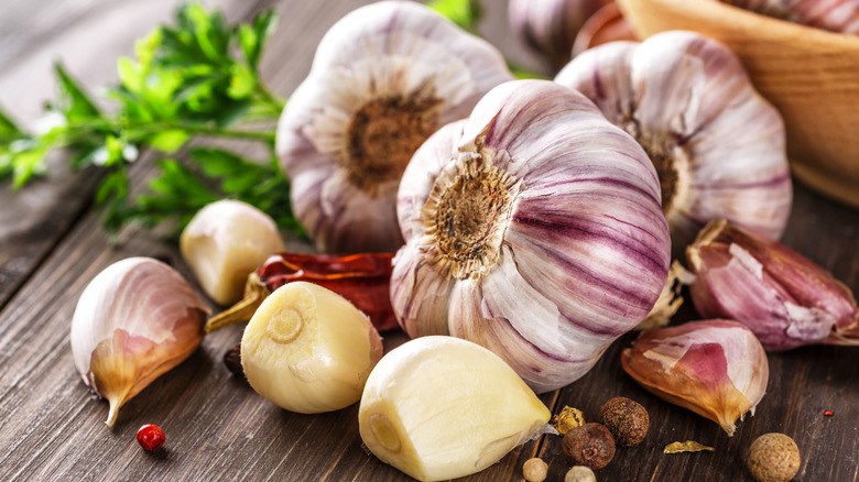 Garlic cloves and bulbs on wood surface with herbs in the background.