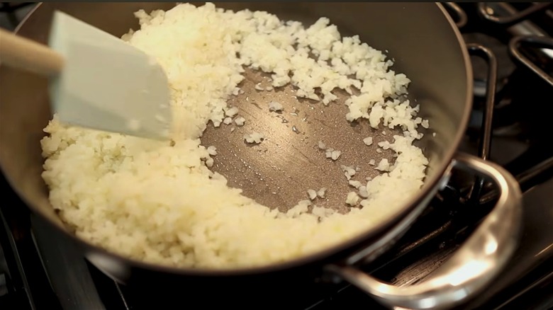 Cauliflower rice being cooked with a small amount of oil.