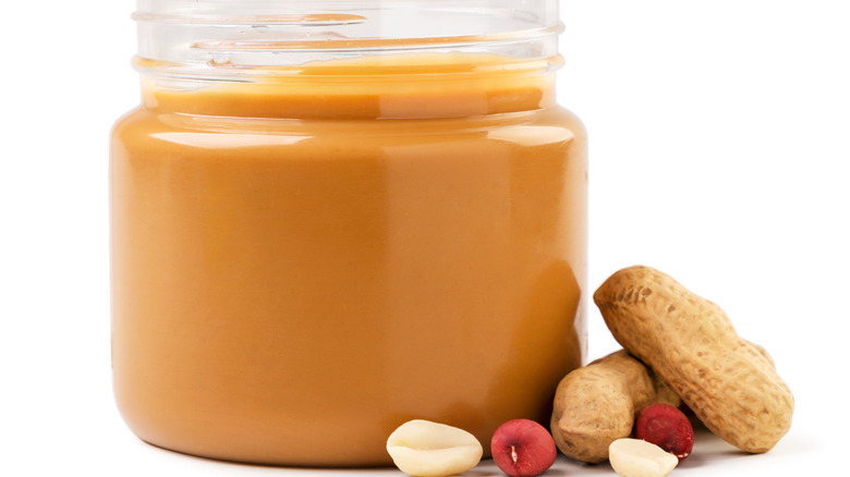 A jar of natural peanut butter with peanuts around it 