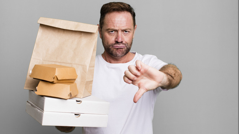 Man giving a thumbs down symbol holding fast food boxes and bag
