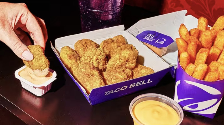 Taco Bell chicken nuggets in a box with a hand dunking a nugget in sauce