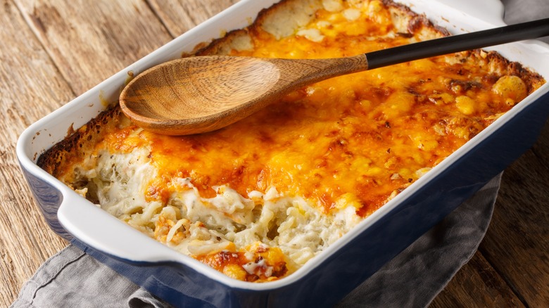 cheesy hash brown casserole in a blue dish with a wooden spoon on top