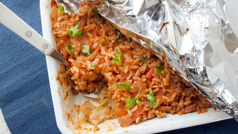 minced meat and rice casserole in a white baking dish that's partially covered in tin foil