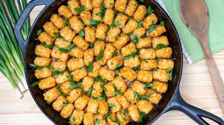 aerial view of a cowboy casserole in a cast iron skillet with a wooden spoon and green onions on the side