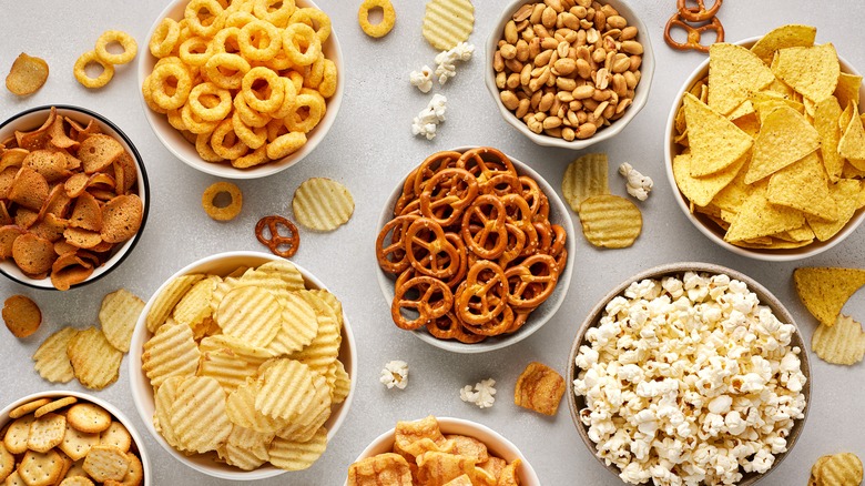 Table with bowls of chips, popcorn, and other snacks