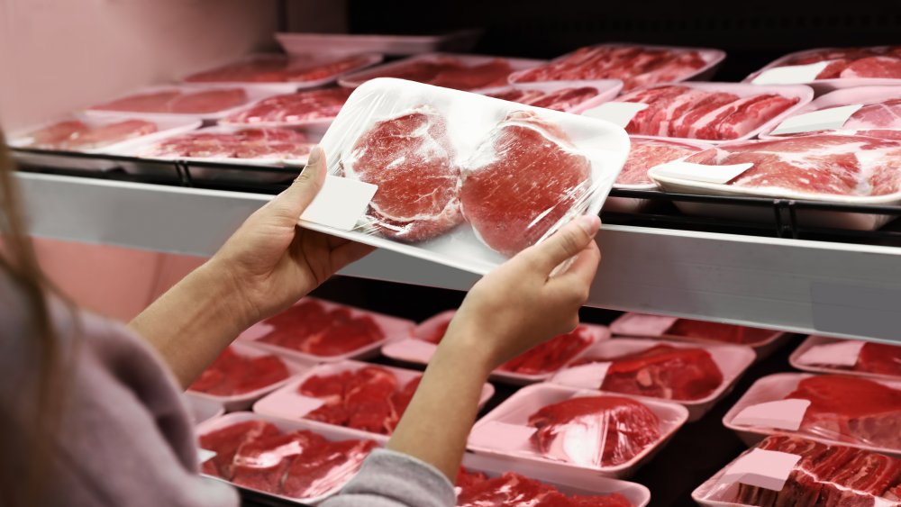 woman holding a package of meat at grocery store