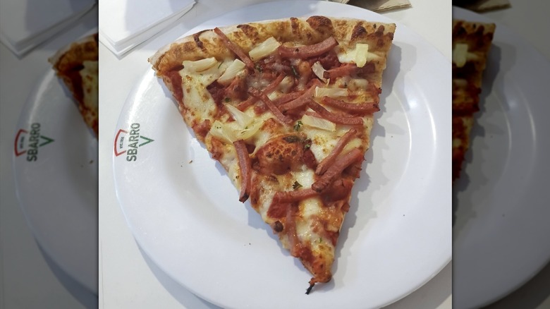 A slice of Sbarro pizza with ham and pineapple on a white plate