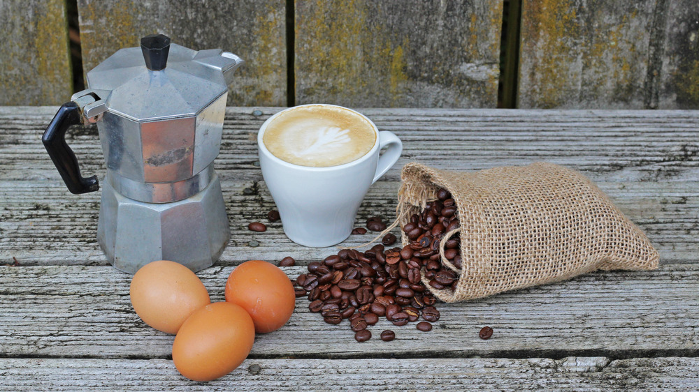 Coffee maker, coffee beans, and brown eggs setting on a wood table