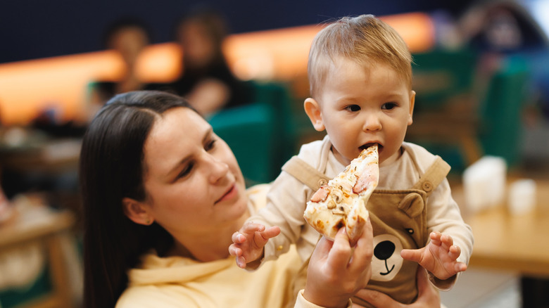 Child biting a slice of pizza, being held by parent