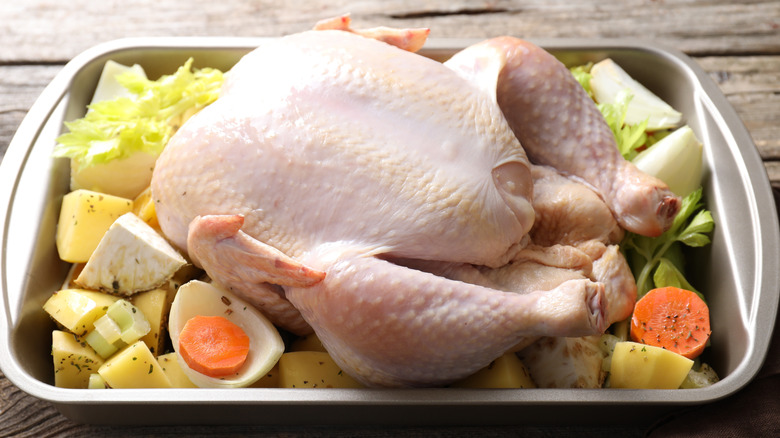A baking tray with one whole, raw chicken on a bed of seasoned veggies