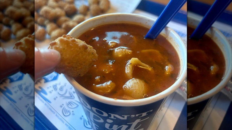 Person dipping a cheese curd into Culver's Tomato Florentine Soup in a to-go cup
