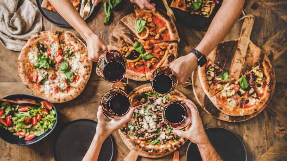 People reaching over table full of pizzas