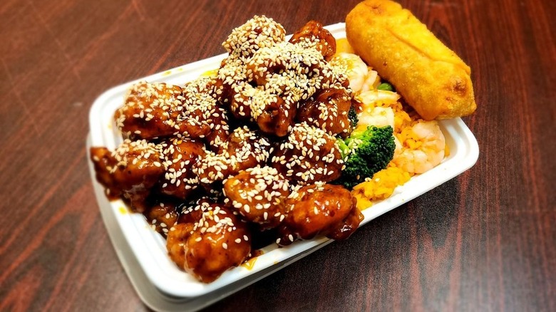 Sesame chicken shrimp fried rice and an egg roll on a to-go platter