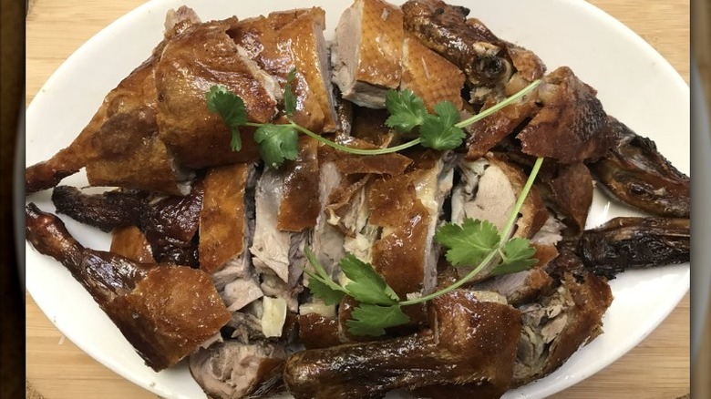 Whole roast Chinese duck on a white platter garnished with parsley leaves