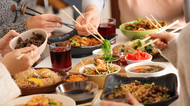 People enjoying a variety of Chinese dishes spread out on a table with chopsticks
