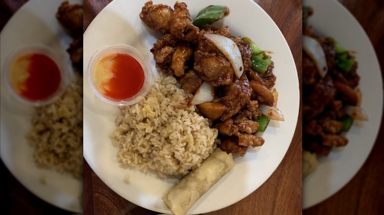 General Tso's chicken with rice and an egg roll on a white plate
