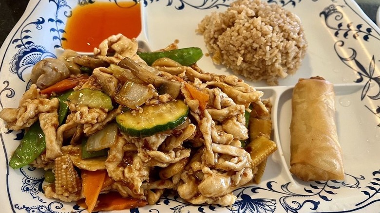 Schezwan chicken lunch with rice and an egg roll on a white plate with blue decorations