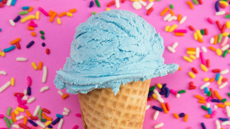 sugar cone of blue ice cream in front of backdrop of rainbow sprinkles
