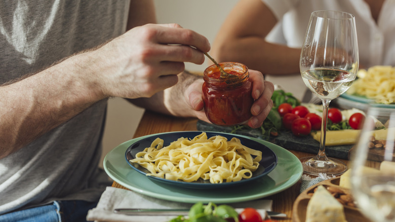 Person spooning jarred tomato sauce onto their pasta