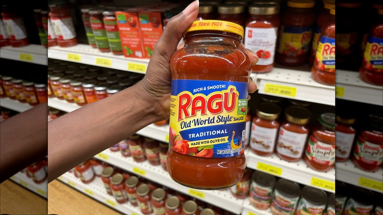 Person holding jar of Ragu brand pasta sauce in grocery store