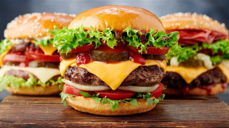 Three juicy hamburgers with pickles, cheese, tomato, curly leaf lettuce, mayo, and more