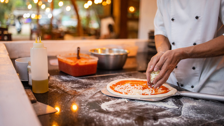 chef adding cheese to uncooked pizza dough