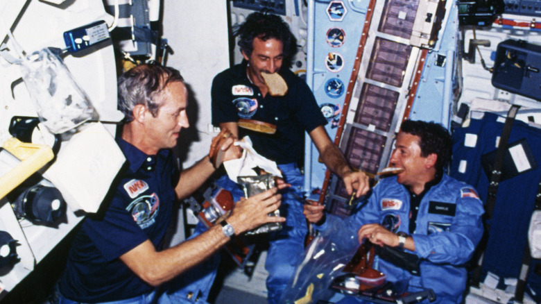 Three astronauts eating in a space shuttle