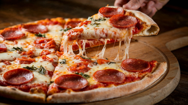 Person taking pizza slice from cutting board