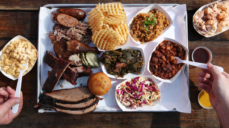 An overhead shot of barbecue foods including meats, waffle fries, mac and cheese, collard greens, rice, coleslaw, and baked beans.