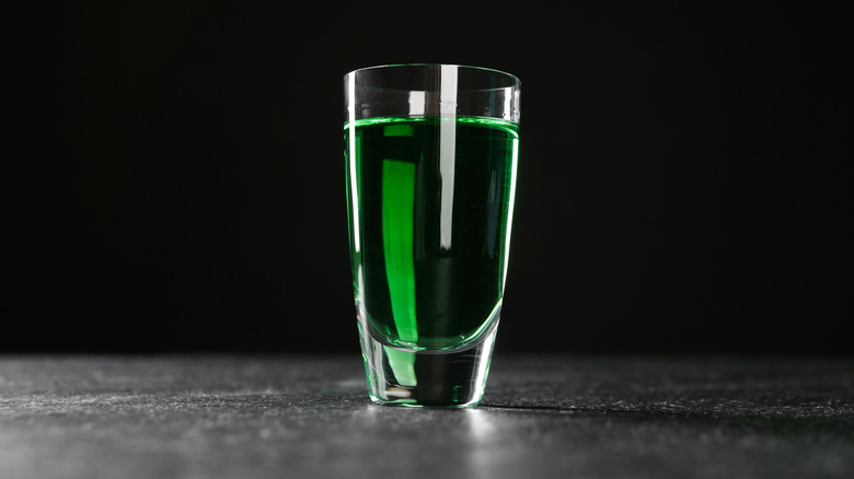 A shot glass full of vivid green absinthe