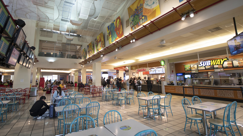 A mall food court full of tables with restaurants spreading down the aisle.