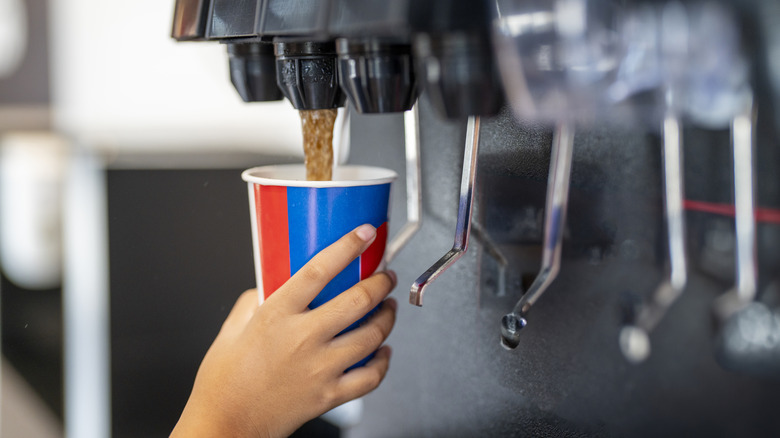 Person dispenses soda into cup from machine