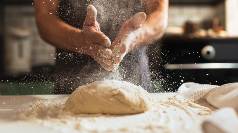 Baker tossing flour on a loaf of bread