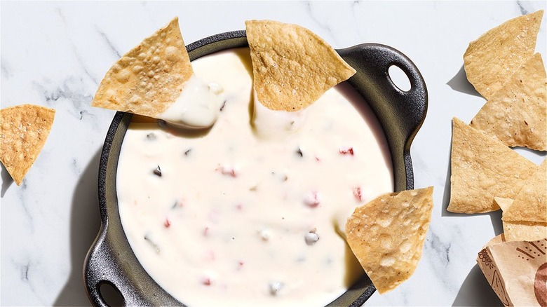 A skillet with queso blanco dip with peppers on it, with some tortillas on the side 